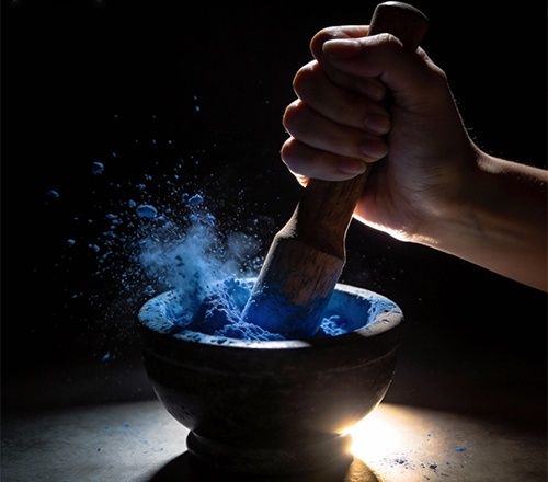 Hand grinding vivid blue pigment in a dark stone mortar